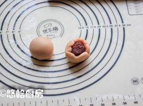取一个面团将2头向内按压，擀开包入豆沙馅，用虎口向上推的方式收好口，捏紧收口。