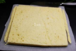 .烤好的面包倒扣在另一张硅油纸上，并把垫在烤盘上硅油纸撕去，让面包快速冷却之后，将面包的四边切去，使面包成为规则的方形，等会卷的时候好看。