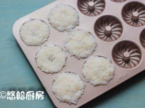 戴一次性手套将米饭放入甜甜圈蛋糕模具中，压紧压实，因为要给小朋友吃，米饭里没有放寿司醋。
