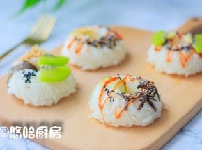 将模具倒扣在案板上，饭团就是完整的甜甜圈形状，用黄瓜片、海苔片从饭团中间缠一道，在饭团上摆上肉松、猕猴桃、黑芝麻、海苔碎等，淋上番茄沙司装饰一下即可。