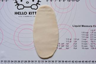 15分钟后进行第一次擀卷：取1个酥皮轻轻压扁，擀成椭圆形薄片