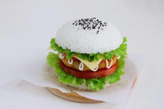 接着放上一片西红柿片、芝士片、生菜，最后把涂抹番茄酱的米饭团盖上，撒少许黑芝麻装饰。