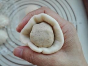 将醒发好的水油皮小剂子，用擀面杖将其擀成圆形面片，放入一个油酥小剂子，将其利用虎口收好接口，如图所示。