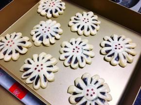 将12片花瓣都扭一下，有豆沙的切面朝上，再用牙签沾上食用红色素，在菊花酥的最中间点上5个小红点，将整形好的豆沙菊花酥放入烤盘里。