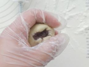 取一份月饼皮用手撑压扁，放入一枚35克的豆沙馅。 利用虎口把馅包好。