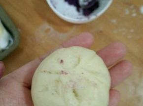 取个大的剂子，放适量紫薯陷，包好并搓成椭圆形。(稍微搓一下，比圆形长一点就好。)然后摆在烤盘里，再取个小剂子搓圆，抹点水，沾到椭圆形包子上方。