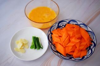 鸡蛋打散备用，胡萝卜去皮洗净先斜段再竖着切片，蒜切片，葱切寸段
