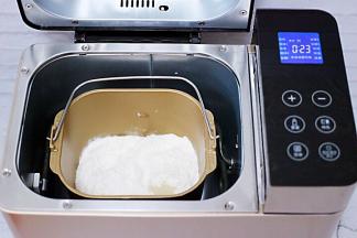 加入奶粉，全蛋液、花生油、再加入高筋面粉和低筋面粉，让面粉覆盖整个上面，面粉的顶端挖个小洞，加入酵母粉，再用旁边面粉把酵母粉盖起来后，启动面包机开始一个和面程序。