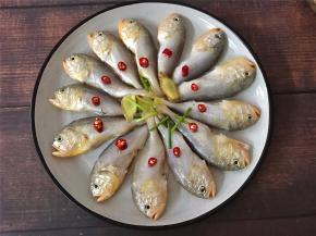 取一盘子下面放上葱白和老姜片，把腌好的梅五鱼摆放在上面。