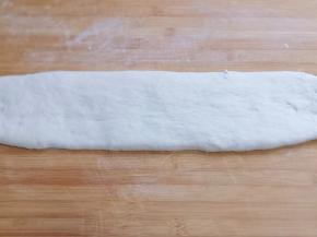 发酵好的面团取出，揉几下排气，不需要大力揉，盖上保鲜膜松弛10分钟，再用擀面杖将面团擀长，如图！