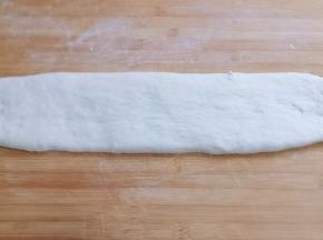 发酵好的面团取出，揉几下排气，不需要大力揉，盖上保鲜膜松弛10分钟，再用擀面杖将面团擀长，如图！