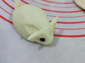然后用拇指和食指在耳朵下面一点的地方，轻轻压下去，再沾上红豆做眼睛。
