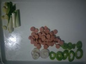面团醒发期间，准备下蔬菜部分:葱切长段，蒜切片。火腿肠切成小圆片。圆葱和青椒切圈。备用