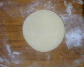 取一个面团。按扁，用擀面杖擀成中间后周边薄的饺子皮状，可撒适量熟糯米粉防粘