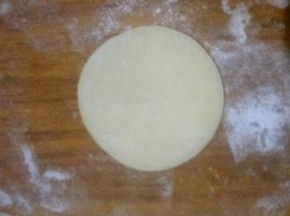 取一个面团。按扁，用擀面杖擀成中间后周边薄的饺子皮状，可撒适量熟糯米粉防粘
