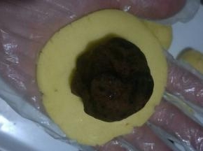 取一个面团，按扁圆，周边薄中间厚一点，放入豆沙馅