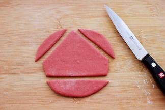 开始做帽子、取一块红色面团揉匀擀成椭圆形薄面片、用刀把多余的部分去掉。