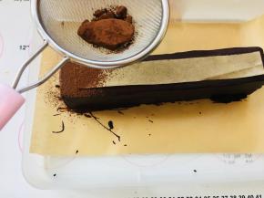 剪一块油纸，大小正好可以位于蛋糕中间，漏出四边。筛上可可粉。