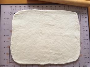 将发酵好的面团拿出排气，盖上保鲜膜松弛15分钟，然后擀成长方形