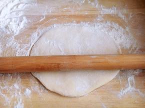 面被擀的薄了些，但是还不太理想，再撒上面粉，用擀面杖卷起面饼继续再擀。