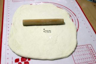 把发酵好的面团，挤出面团内的空气，揉搓成光滑面团，用擀面杖擀成长方形（长椭圆形也可以），擀面的时候，要尽可能把面团里的气泡擀出来。