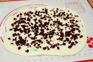 擀开的面团上面均匀撒上蔓越莓紫薯馅。蔓越莓紫薯的做法，把紫薯蒸熟去皮，放白砂糖炒至溶解，分3次倒入油均匀炒至完全吸收，最后把蔓越莓干加入炒均即可。