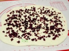 擀开的面团上面均匀撒上蔓越莓紫薯馅。蔓越莓紫薯的做法，把紫薯蒸熟去皮，放白砂糖炒至溶解，分3次倒入油均匀炒至完全吸收，最后把蔓越莓干加入炒均即可。
