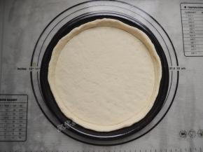 披萨盘刷一层薄油，将圆形面饼放入披萨盘中，用手压薄底部，使中间薄边缘厚。