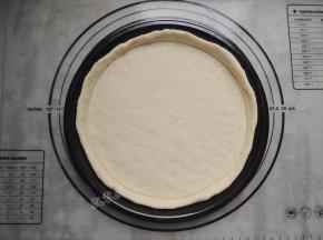 披萨盘刷一层薄油，将圆形面饼放入披萨盘中，用手压薄底部，使中间薄边缘厚。