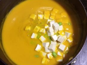 南瓜糊倒入锅里，小火加热。如果南瓜糊太稠请适量加点水，反之请大火加热，收干水份至你想要的浓稠度。
南瓜糊煮开后放入豆腐和毛豆