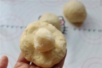 取一个小剂子，按扁后包入椰蓉馅，包起来，并捏紧收口。