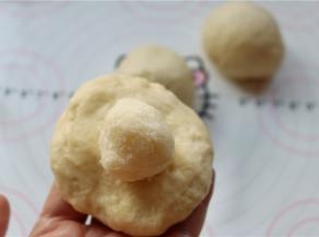 取一个小剂子，按扁后包入椰蓉馅，包起来，并捏紧收口。