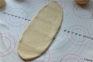 取一个包入椰蓉的面团，按扁后擀成牛舌状，尽量窄长一点。