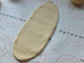 取一个包入椰蓉的面团，按扁后擀成牛舌状，尽量窄长一点。
