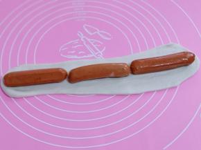 将三分之一的面团擀成长舌状，放上香肠，再卷起来！再切出大小一样的香肠段！