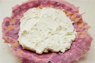 取一个饼皮，有烙痕的一面向上，中间抹上打发好的淡奶油，边缘不要抹。