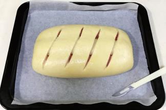 面团发至两倍大时取出，给面包表面刷上一层薄薄的鸡蛋液，用割包刀在表面划几道口。