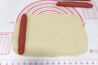 把白色的面团擀成长约30厘米，宽约18厘米的长方形片状，把一根红色长面团放在面片的左边。