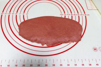 取红色小面团一份，用擀面杖擀成椭圆面片，从上往下卷起，捏紧收口。