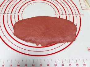 取红色小面团一份，用擀面杖擀成椭圆面片，从上往下卷起，捏紧收口。