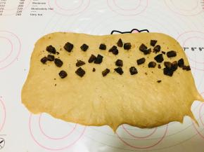 取一个面团，轻压按扁，擀长，翻面！翻面！翻面！将黑糖切成小块，放到面上，底部不放。每个面团黑糖块的量大概20到25克。