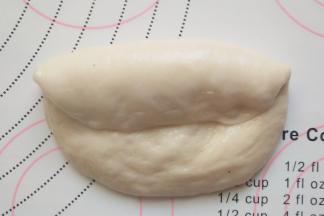 将面团光滑面向下，从面团上边折压三分之一，用掌根摁压边缘至面团上