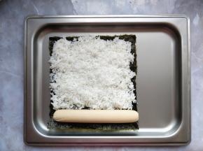 把做寿司用的烤紫菜铺在烤盘上，将拌了少许寿司醋和芝麻油的米饭平铺在上面，压实压平。一端放一根香肠。（我用的是半根香肠，因为一张烤紫菜面积比较小。如果用比较大张的，可以将米饭铺满，再在两端各放上整根香肠）