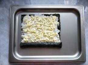 把一端的香肠卷起来，接口在米饭上压实。在米饭上撒少许马苏里拉奶酪碎。