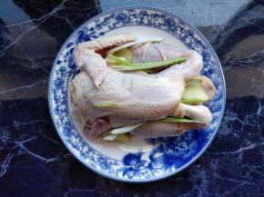 三黄鸡清洗干净后，将葱姜塞入鸡腹中，装在盘中。