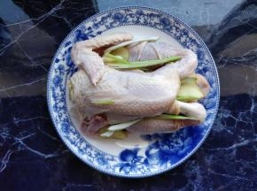 三黄鸡清洗干净后，将葱姜塞入鸡腹中，装在盘中。