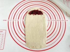 取一份松弛好的面团，用擀面杖擀成长方形，取8克蔓越莓碎放入面片顶端，轻轻压一下。