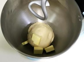 揉至面团光滑，呈扩展阶段，往搅拌桶内加入黄油。