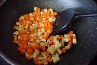 锅里热油后倒入土豆和胡萝卜丁炒出香味