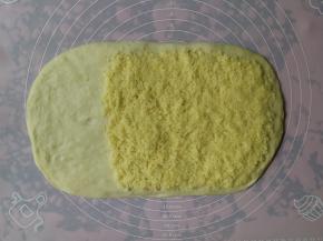 一发完成的面团倒在揉面垫上，用手按压排气后擀成长方形，然后将椰蓉馅料平铺在面团的2/3处，留1/3不铺馅料